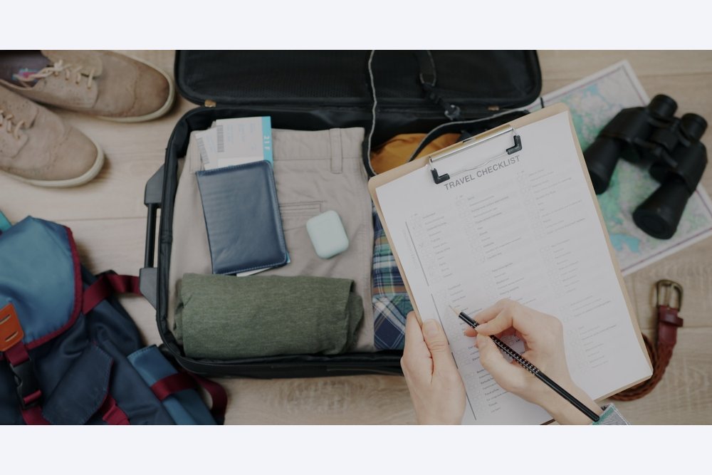 Close-up of travel checklist and packed suitcase and female hand checking items getting ready for trip. Tourism and baggage preparation concept.