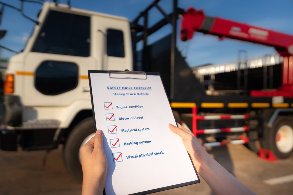 Action of mechanic worker is using the daily checklist form to verify and inspection a heavy truck vehicle (blurred background). Industrial safety working concept photo. Close-up and selective focus.